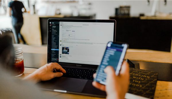 Person holding mobile device and typing on laptop